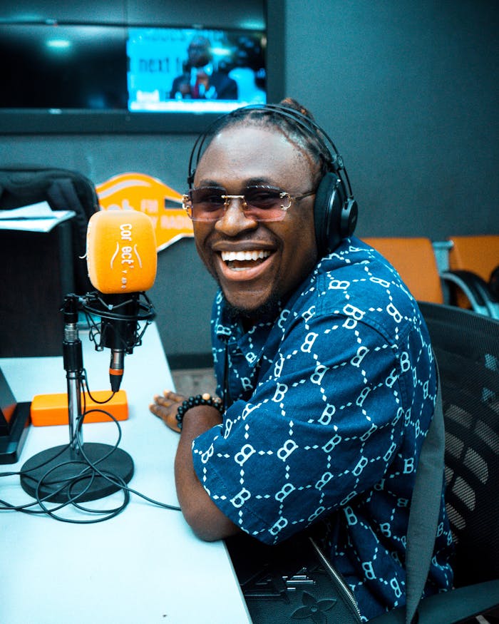 Smiling man wearing headphones speaks into a microphone at a radio studio.