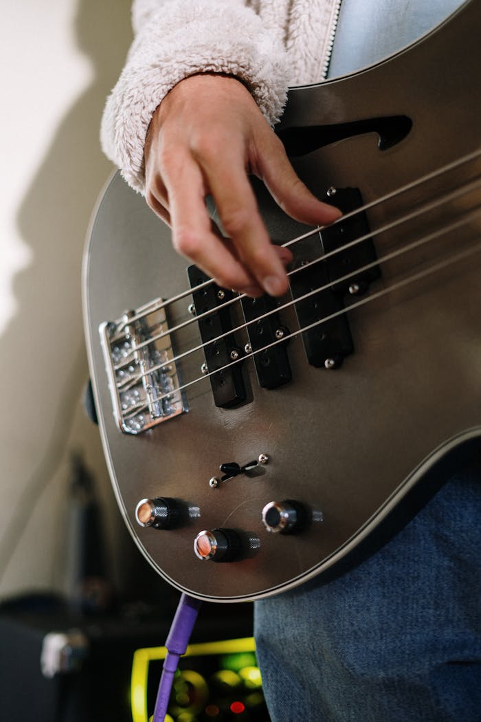 Detailed shot of a hand playing an electric bass guitar in a cozy home studio environment.