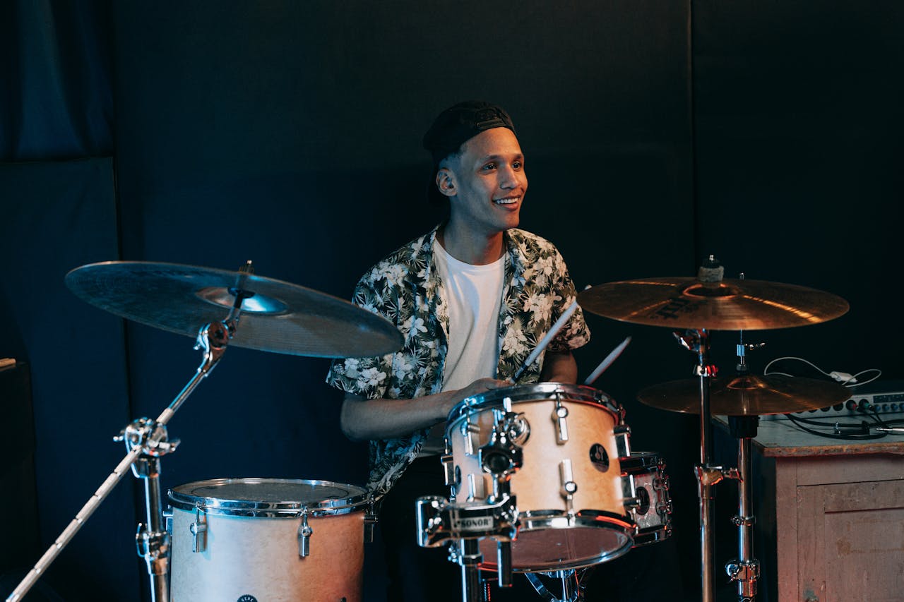 Smiling young adult playing drums in a music studio setting.